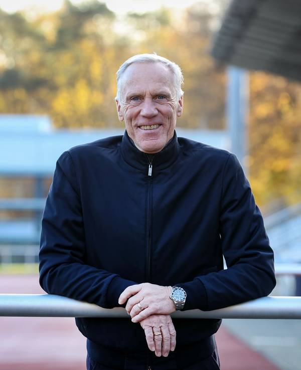 Ingo Froböse lehnt sich im Stadion der Sporthochschule Köln über eine Barriere und schaut in die Kamera.