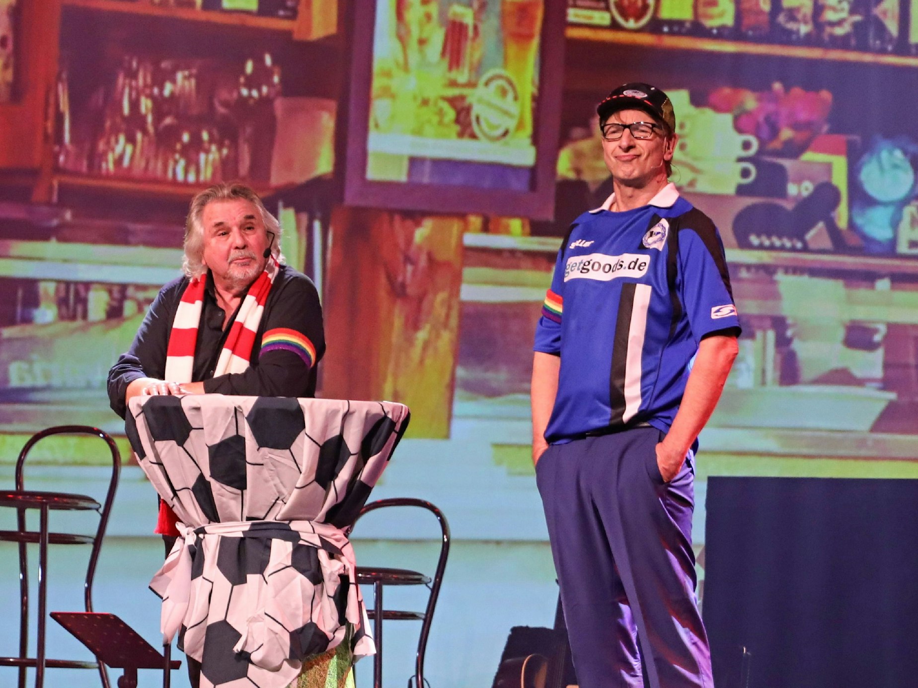 Tommy Engel (l.) und Ingolf Lück auf der Bühne mit Fußball-Trikot und Regenbogenbinde.