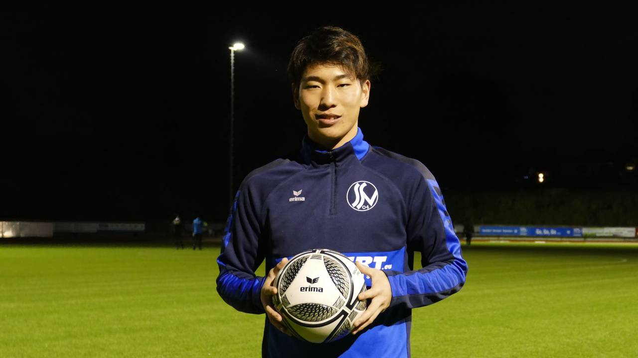 Kaito Asano vom Siegburger SV 04 steht mit einem Fußball in der Hand am Spielfeld.