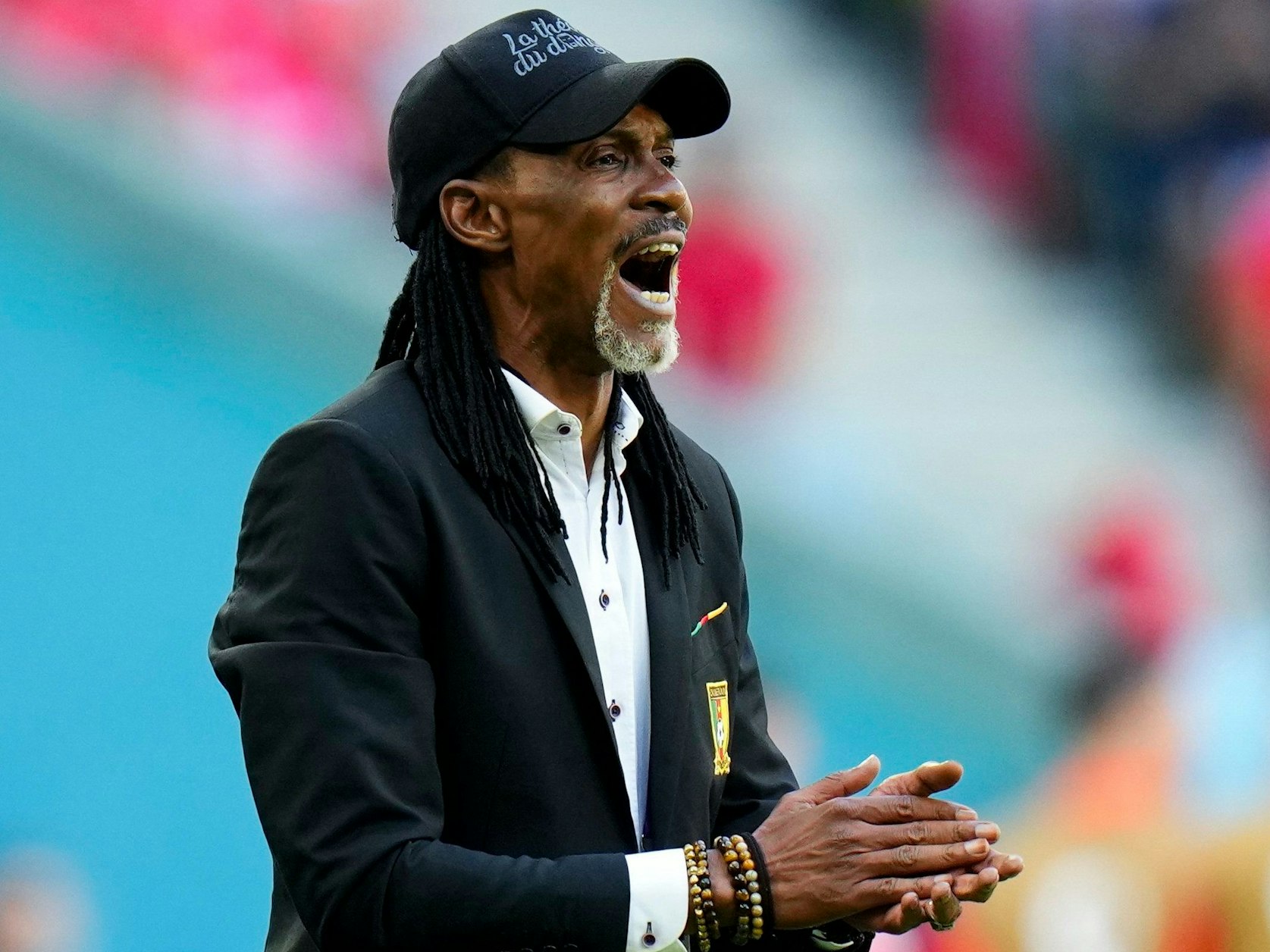 Kameruns Trainer Rigobert Song steht mit Anzug und Cap am Spielfeldrand und klatscht in die Hände.