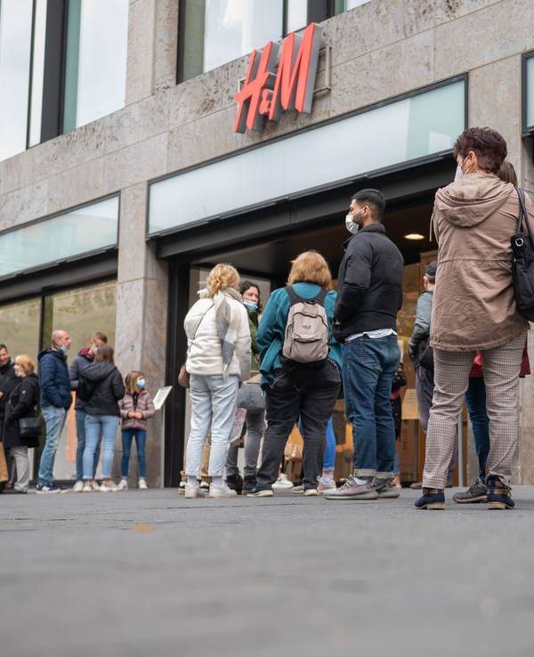 Kundinnen und Kunden stehen in einer Schlange vor einer H&M-Filiale.