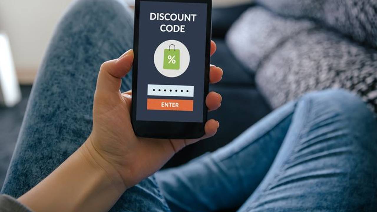Hand hält Smartphone hoch mit Coupon auf dem Screen.