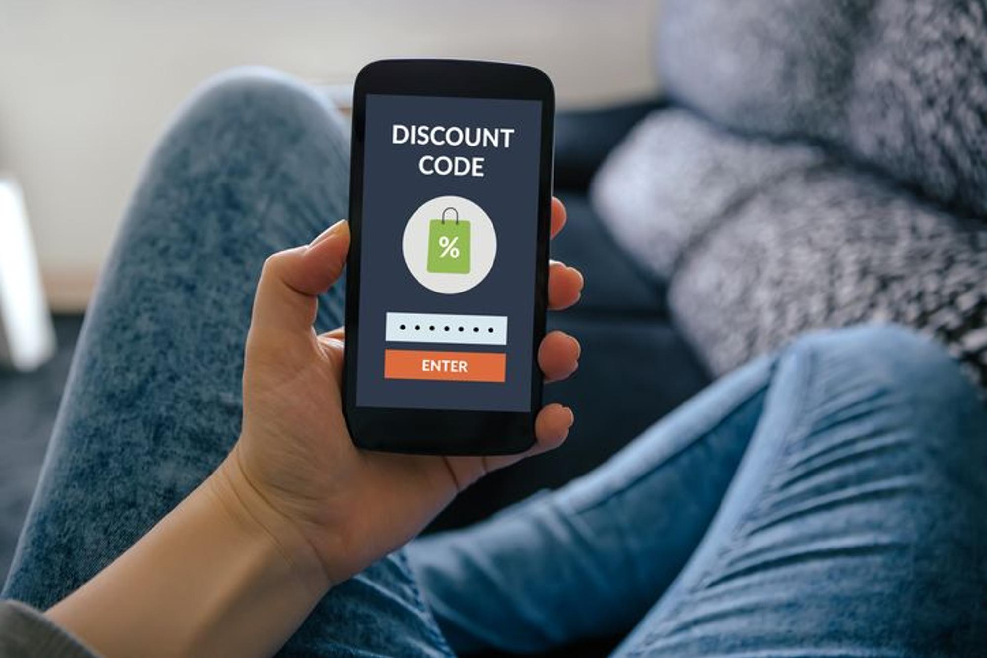 Hand hält Smartphone hoch mit Coupon auf dem Screen.