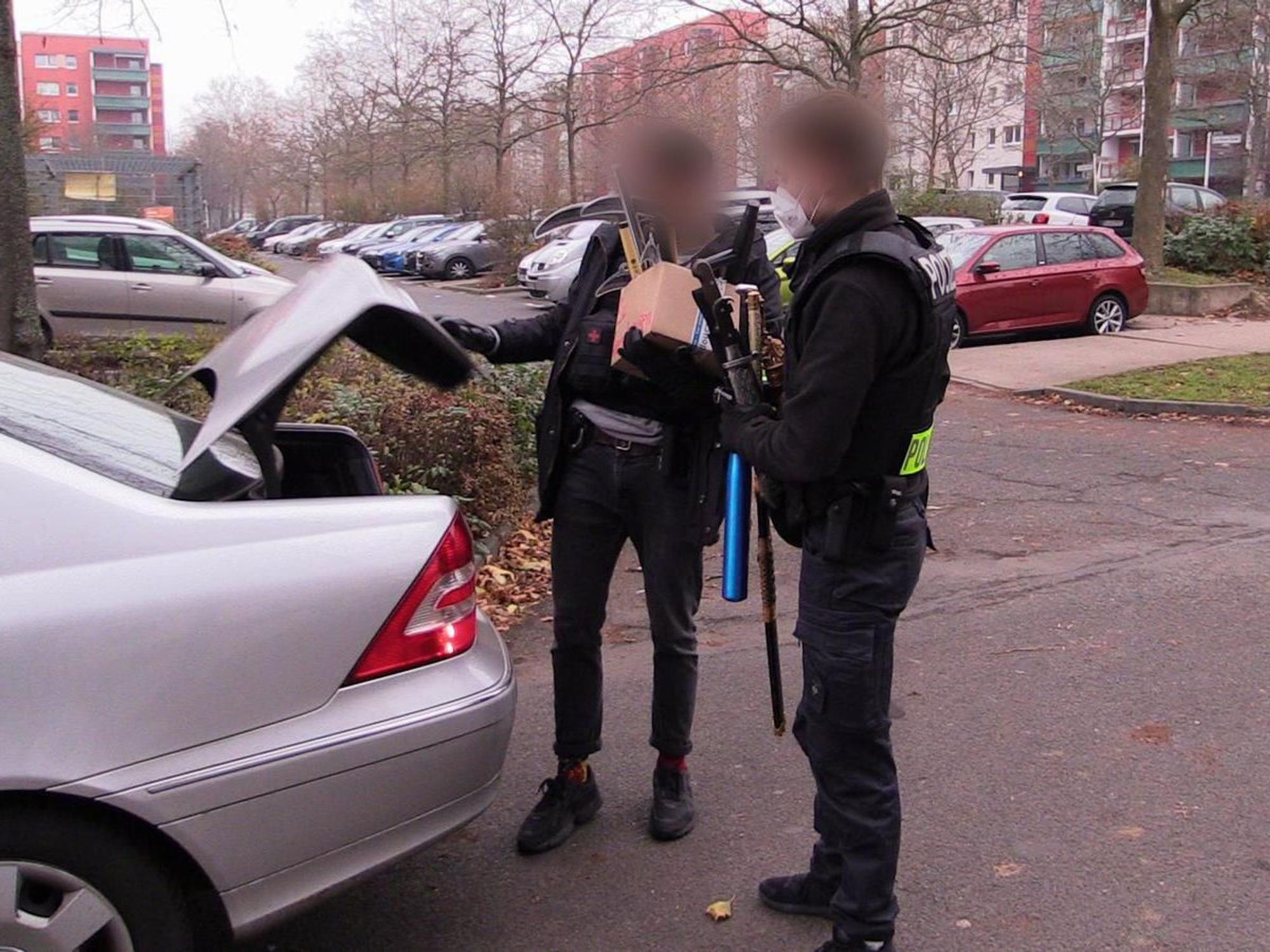 Polizisten verlassen mit beschlagnahmten Gegenständen nach einer Durchsuchung ein Haus.