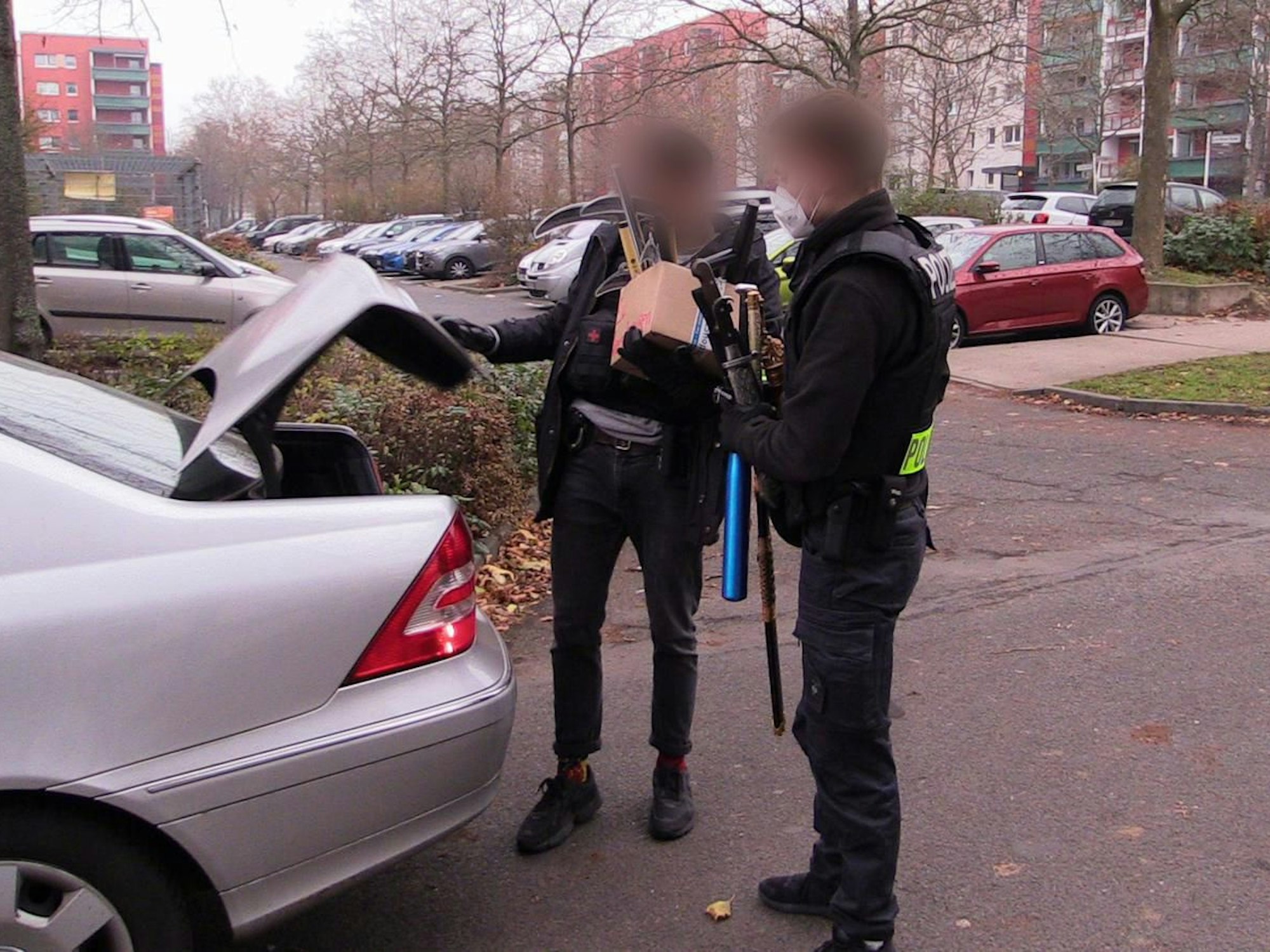 Polizisten verlassen mit beschlagnahmten Gegenständen nach einer Durchsuchung ein Haus.