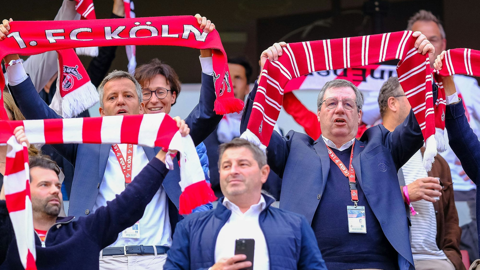 Werner Wolf und Philipp Türoff stehen beim Heimspiel des 1. FC Köln auf der Tribüne und singen die Hymne.