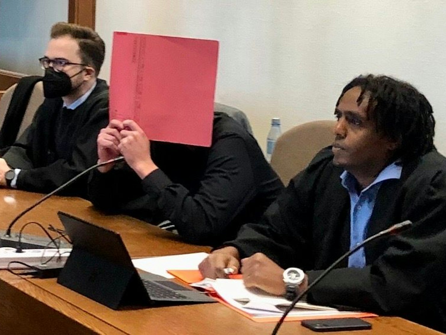 Ein Mann sitzt auf der Anklagebank im Gericht und verdeckt sein Gesicht mit einem Ordner.