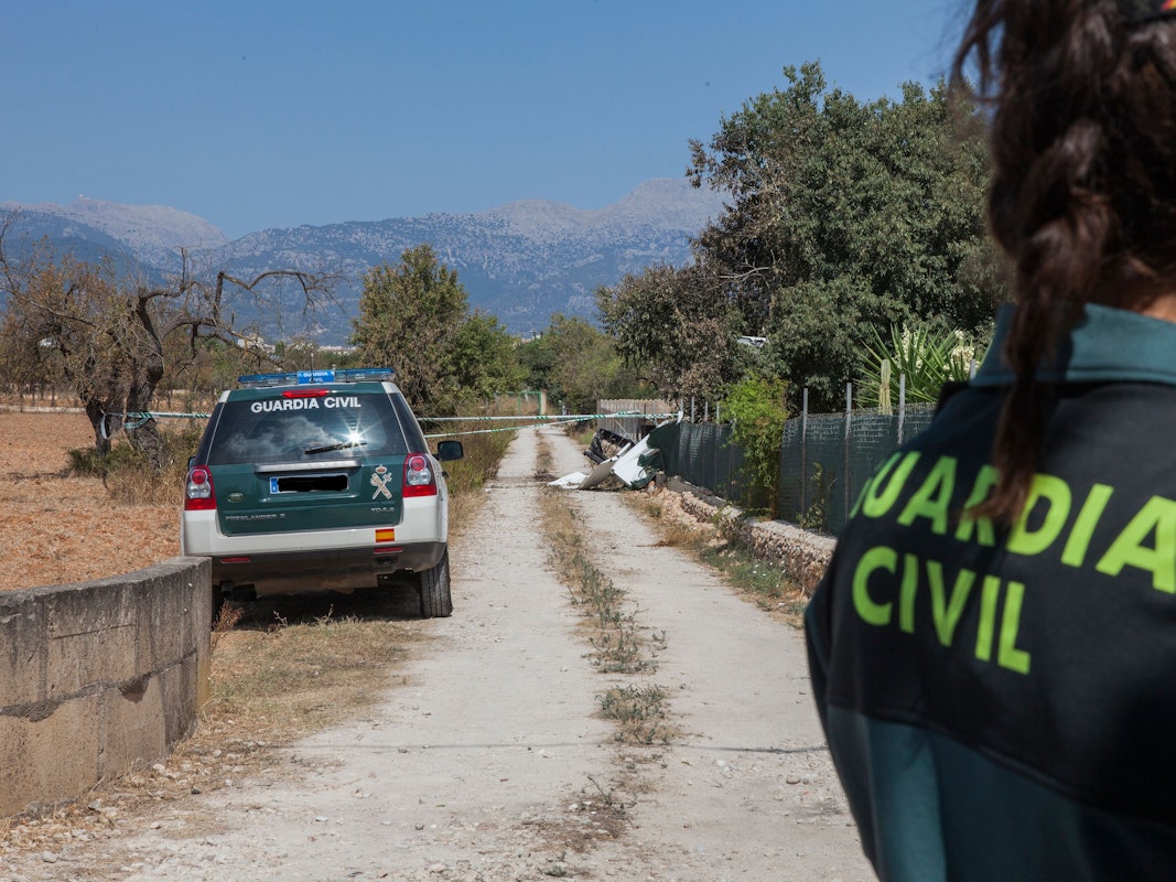 Ein Mitglied der Polizeieinheit „Guardia Civil“ steht nahe einer Absturzstelle, an der nach einer Kollision eines Ultraleichtflugzeugs mit einem Hubschrauber hinter Absperrband Wrackteile liegen.