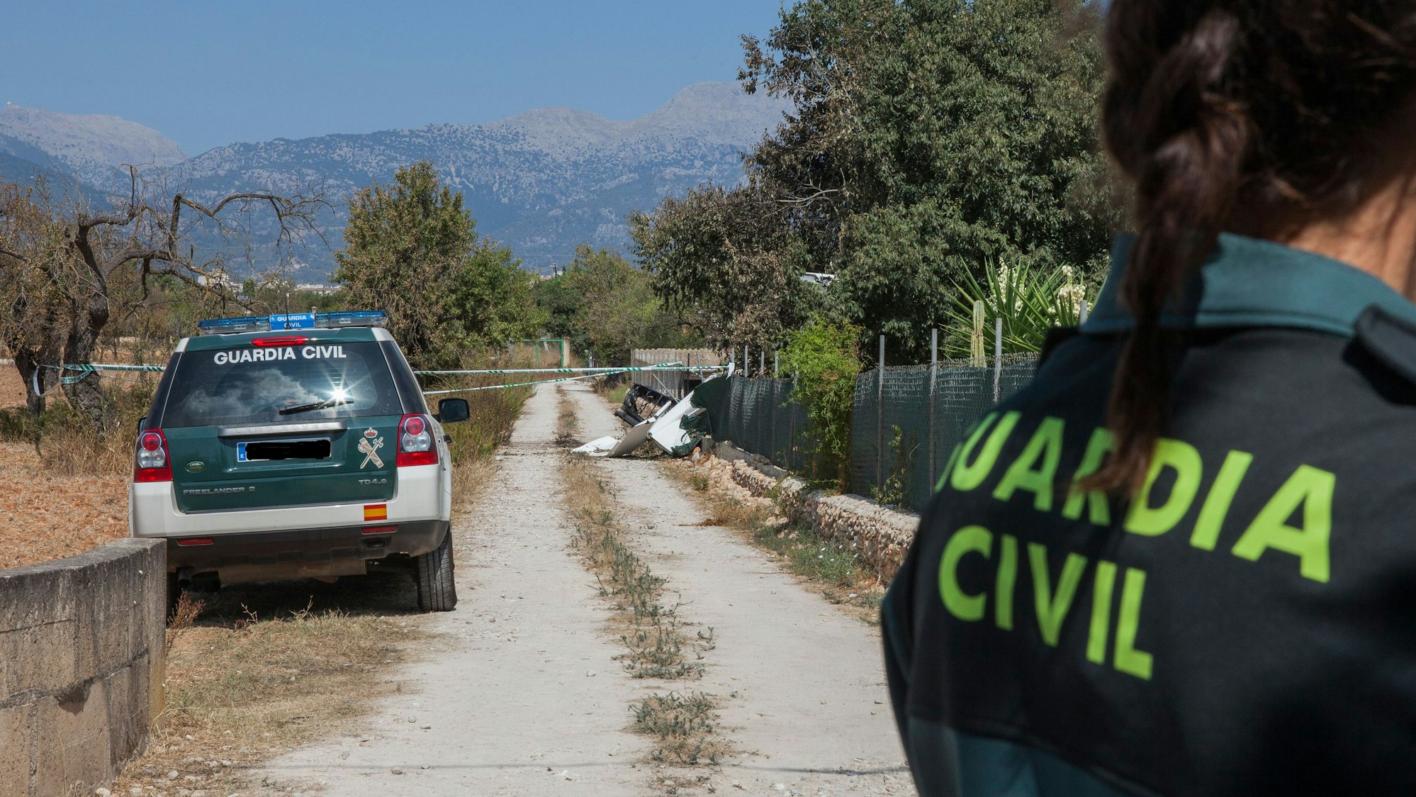 Ein Mitglied der Polizeieinheit „Guardia Civil“ steht nahe einer Absturzstelle, an der nach einer Kollision eines Ultraleichtflugzeugs mit einem Hubschrauber hinter Absperrband Wrackteile liegen.
