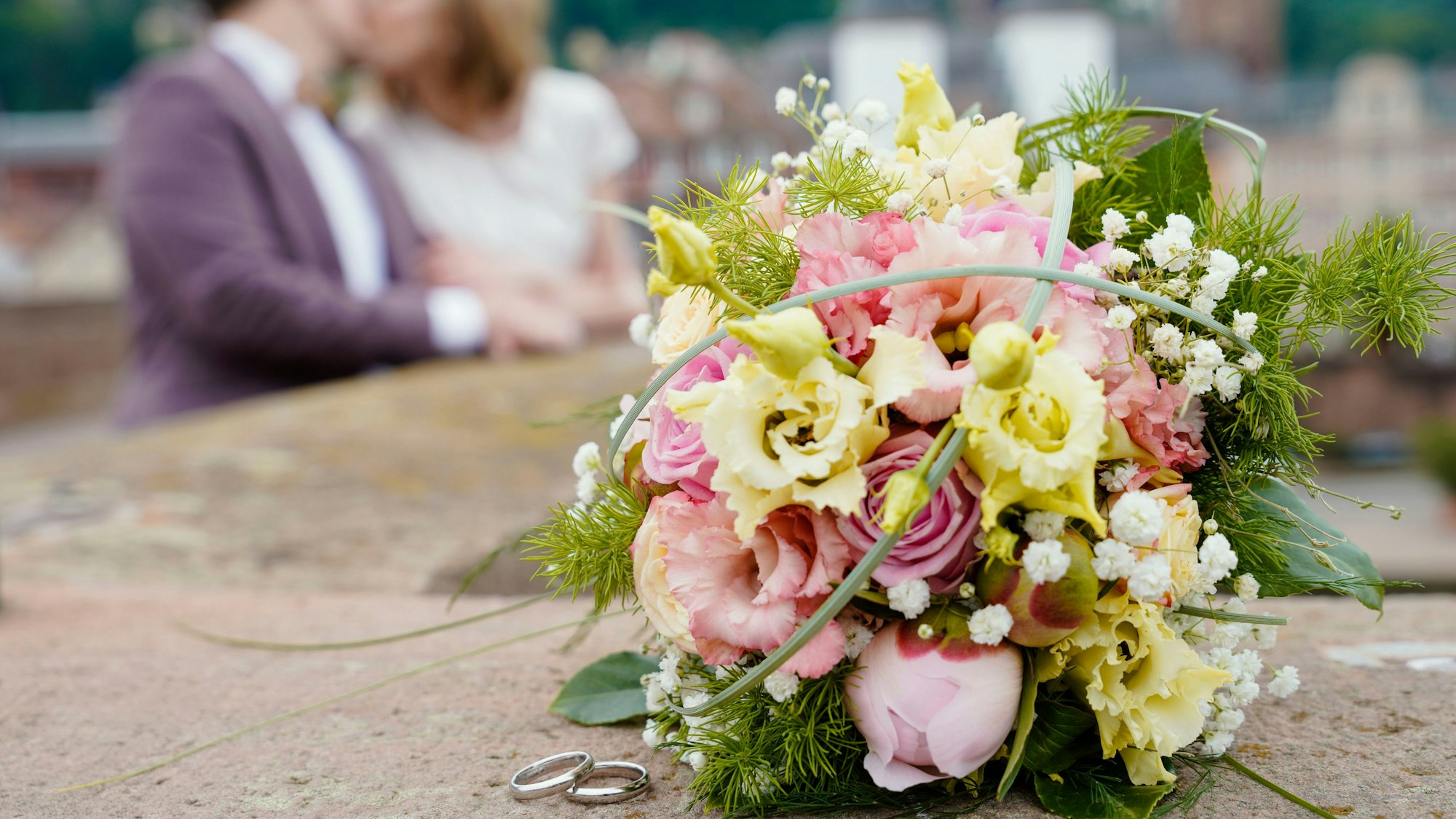 Brautpaar küsst sich auf der Alten Brücke hinter ihrem Blumenstrauß und den beiden Eheringen, die auf dem Brückengeländer liegen.