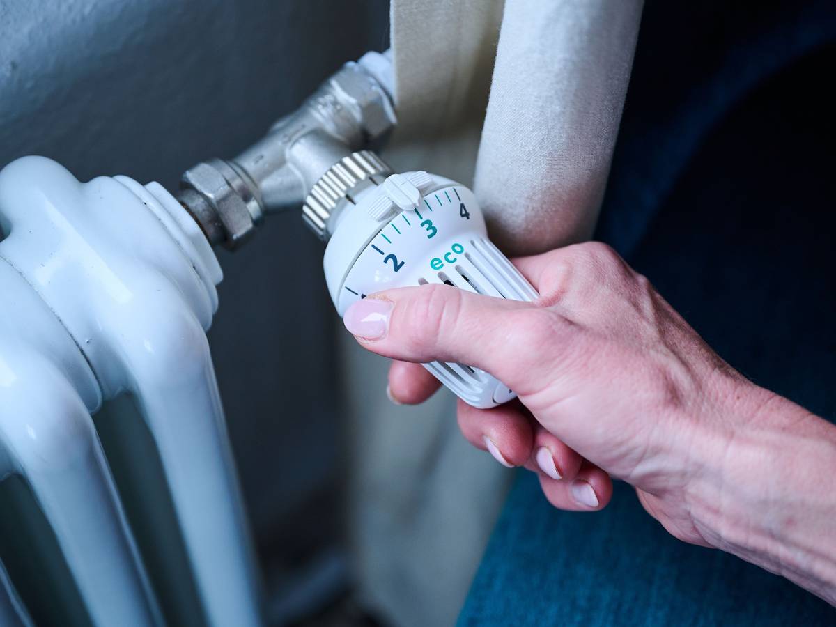 Eine Frau dreht den Temperaturregler einer Heizung auf 3 ("Eco").