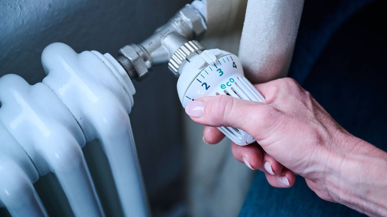 Eine Frau dreht den Temperaturregler einer Heizung auf 3 („Eco“).