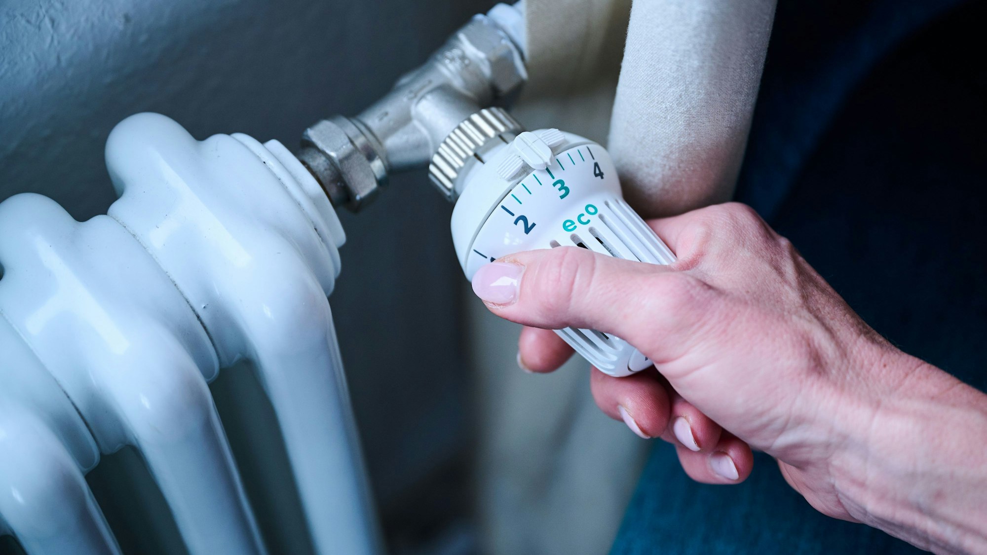 Eine Frau dreht den Temperaturregler einer Heizung auf 3 ("Eco").