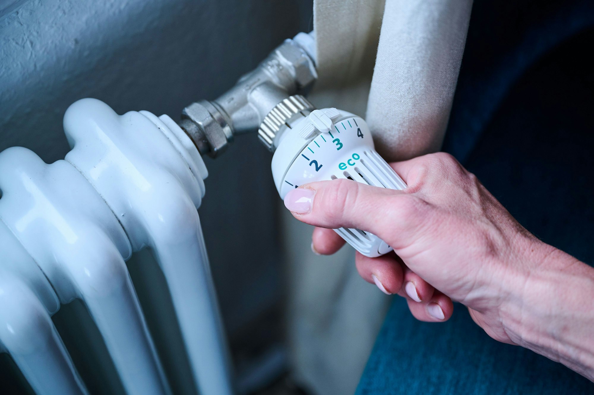 Eine Frau dreht den Temperaturregler einer Heizung auf 3 („Eco“).