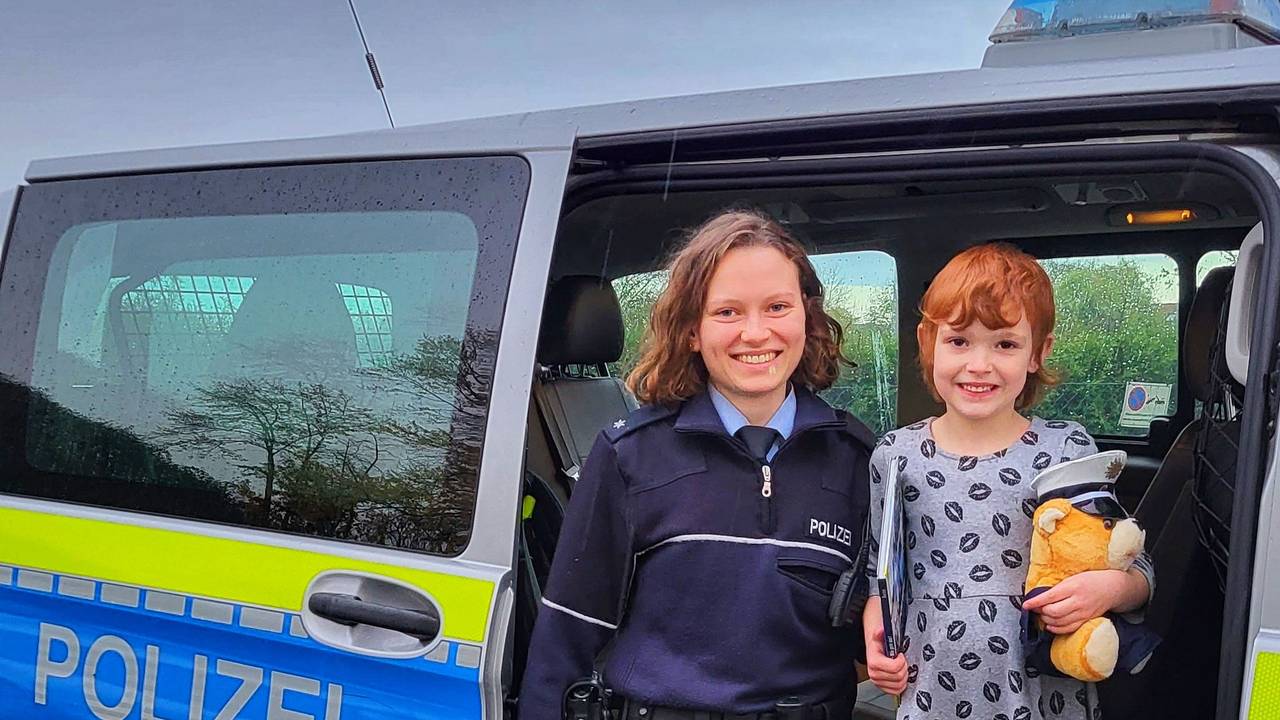 Die kleine Christina steht in einem Polizeiwagen neben einer Polizistin.