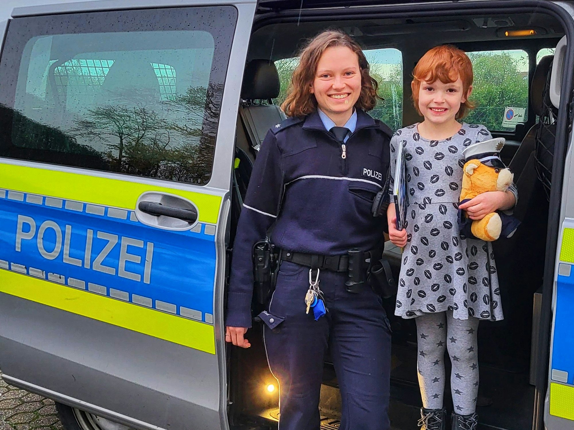 Die kleine Christina steht in einem Polizeiwagen neben einer Polizistin.