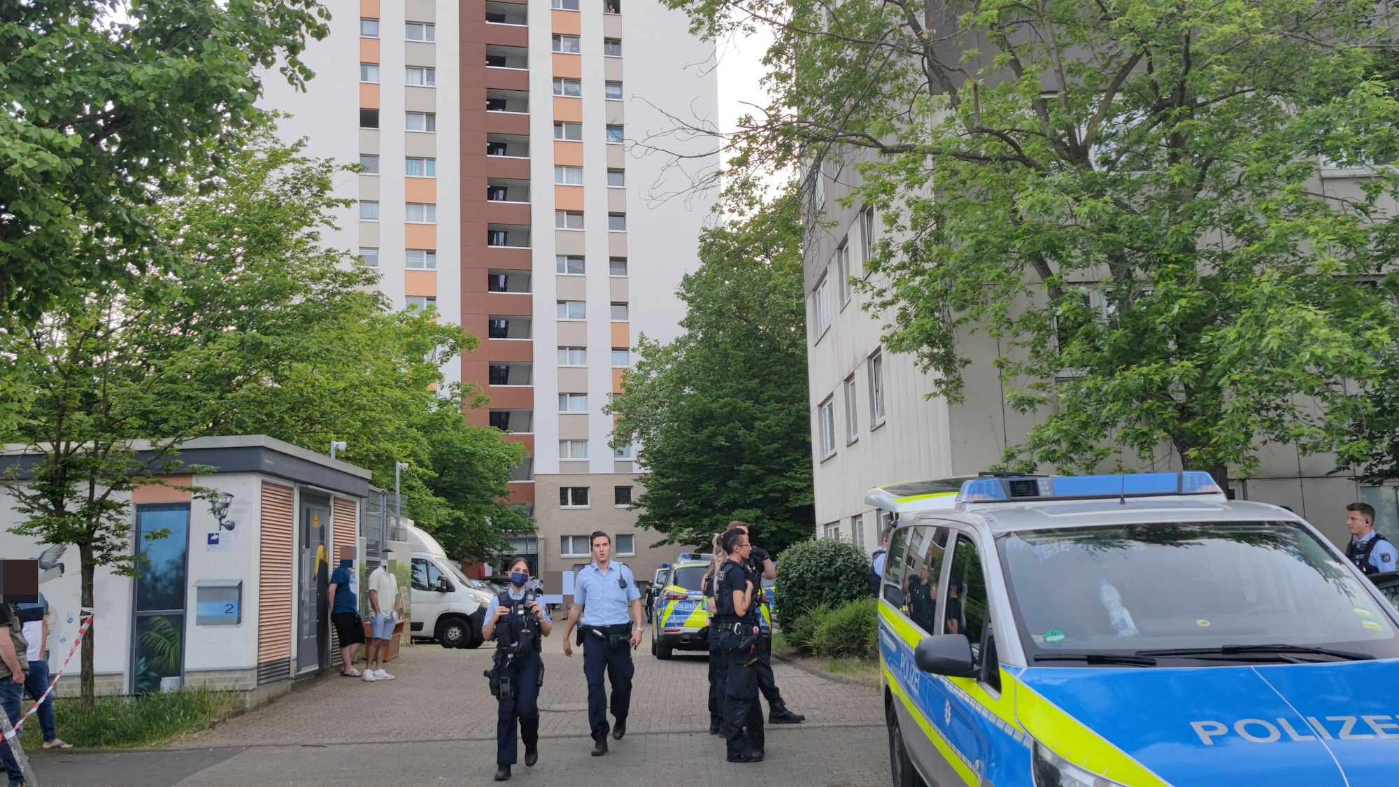 Polizeikräfte stehen vor einem Gebäude in der Gernsheimer Straße in Köln-Ostheim. Neben ihnen steht ein Polizeiwagen.