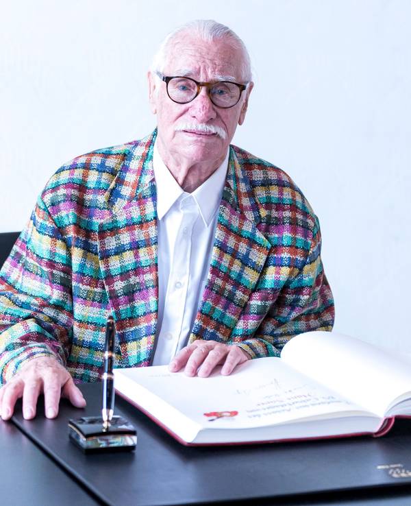 Hans Süper sitzt im Rathaus der Stadt Köln an einem Schreibtisch und hat vor sich das Gästebuch der Stadt liegen.