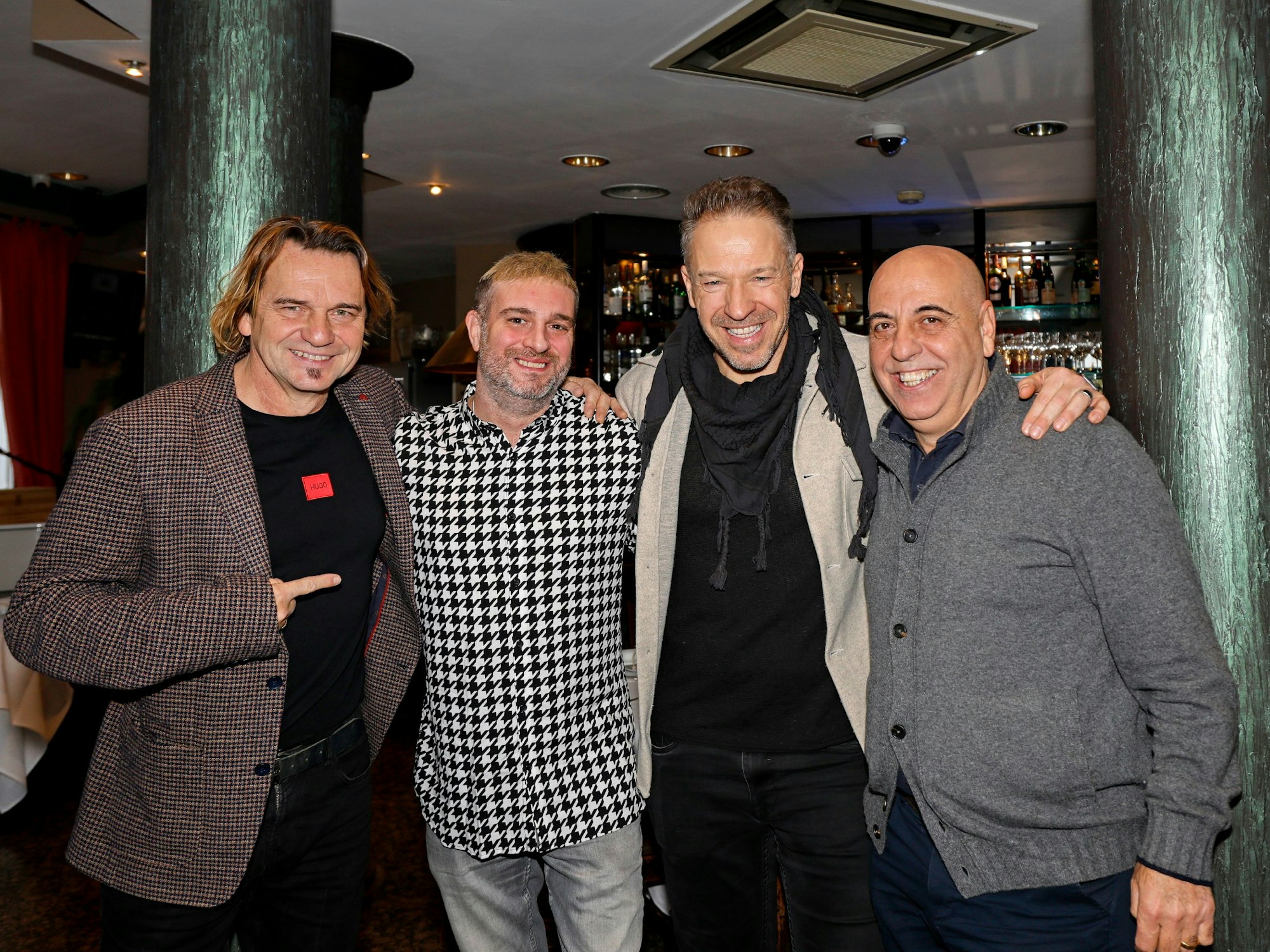 Vier Männer halten sich fröhlich im Arm und lachen in die Kamera.