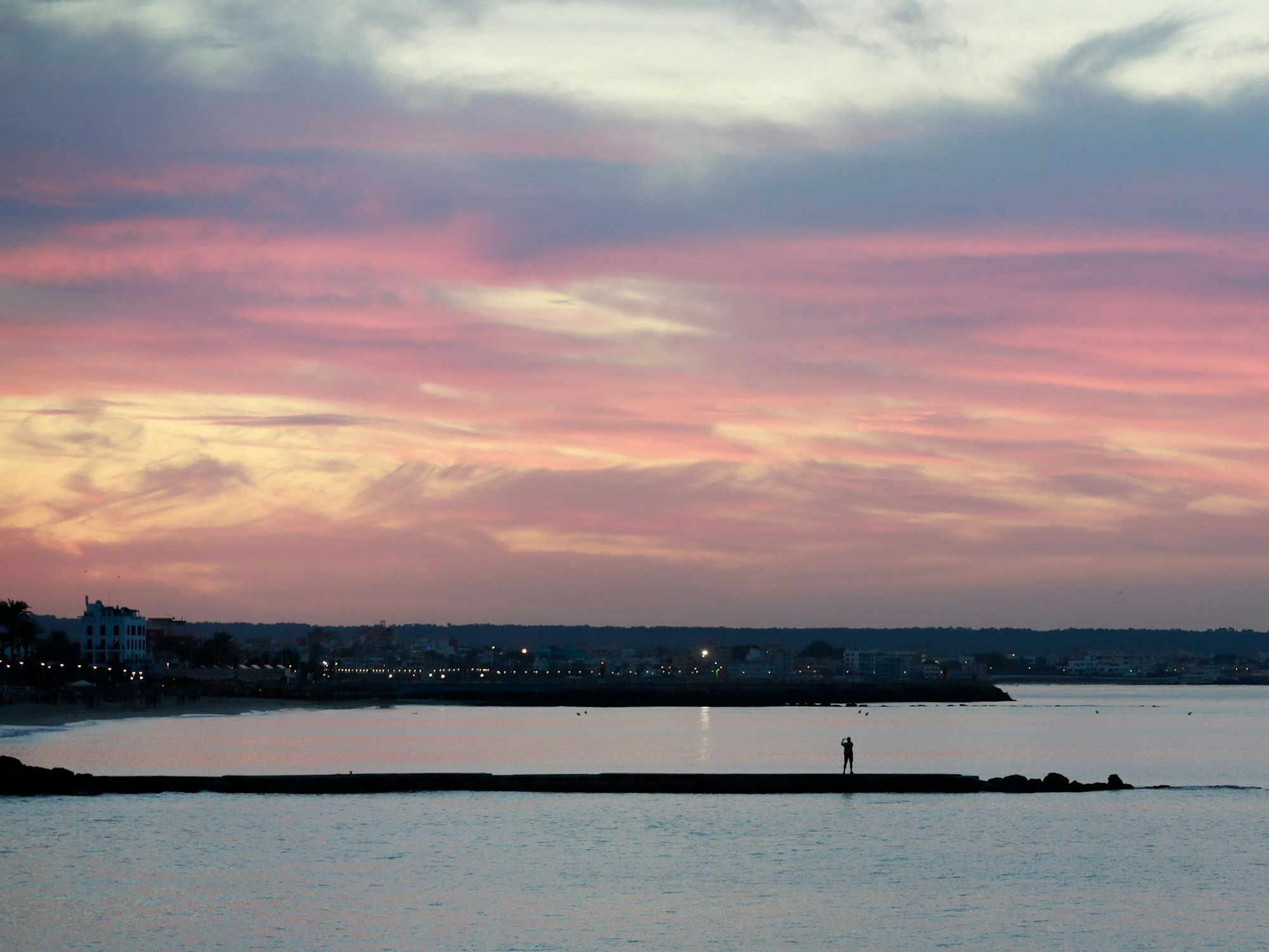 Ein Mann fotografiert mit seinem Mobiltelefon auf einer Mole an der Strandpromenade von Palma im September 2022 den Sonnenaufgang auf Mallorca.