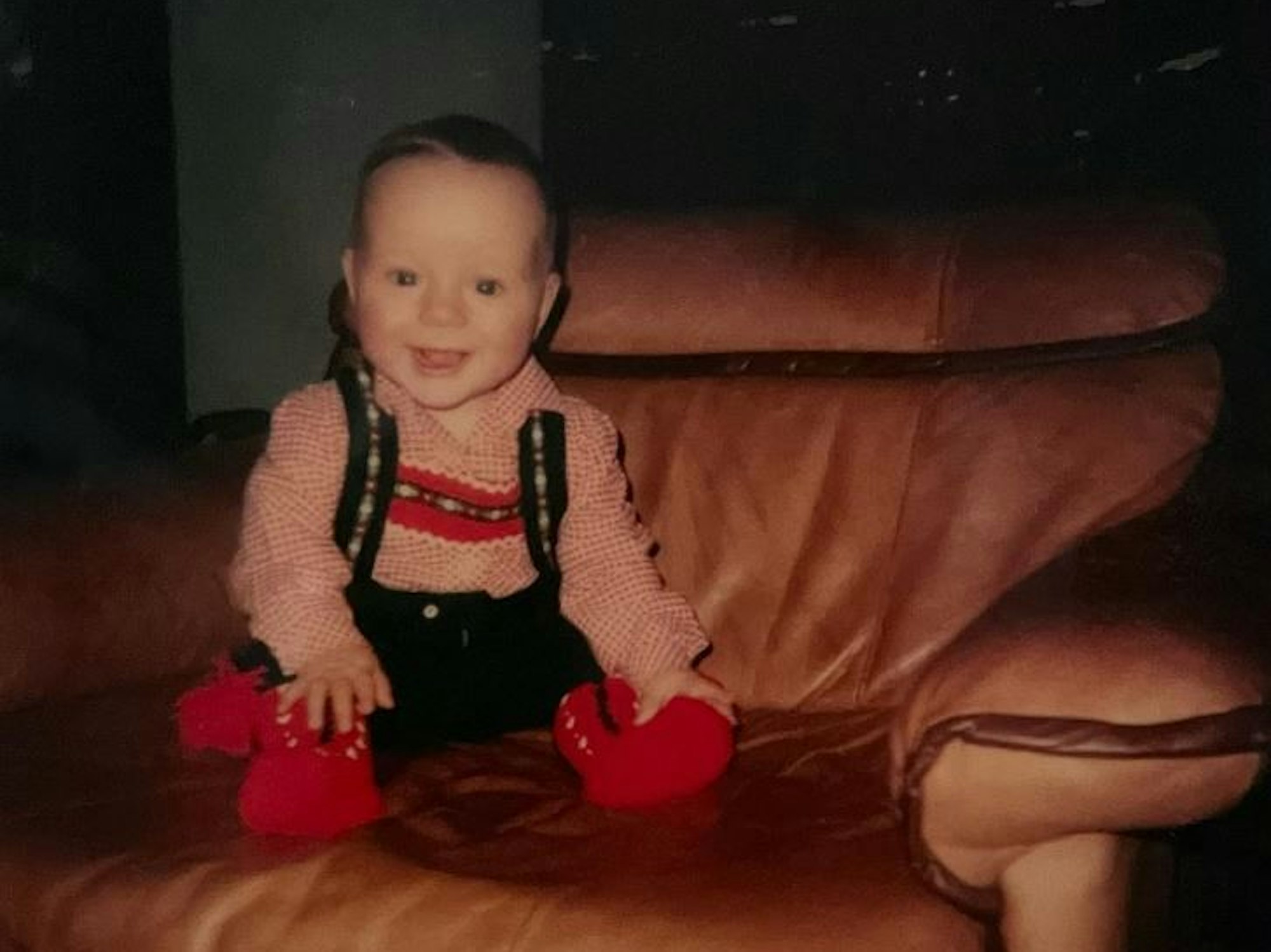 Ein Baby sitzt in einem Ledersessel und hat eine Art Lederhose und Hemd an.