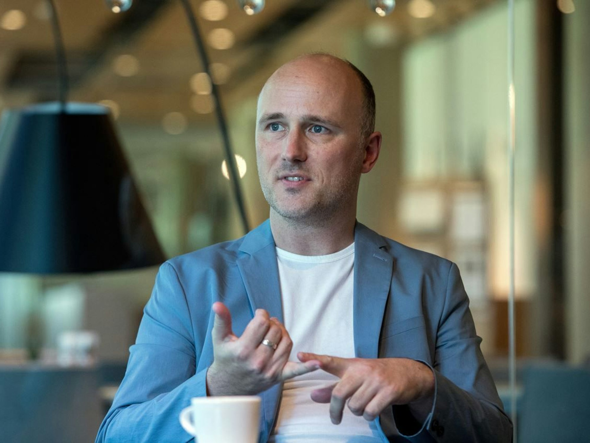 Sven Lehmann sitzt in einem blauen Jackett und weißem Shirt an einem Tisch und gibt ein Interview.