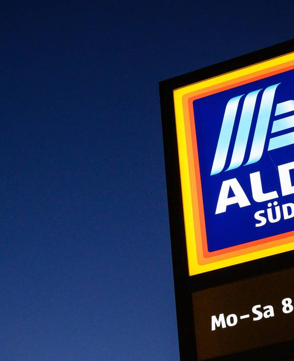 Ein Schild des Discounters Aldi Süd leuchtet in der Dämmerung.