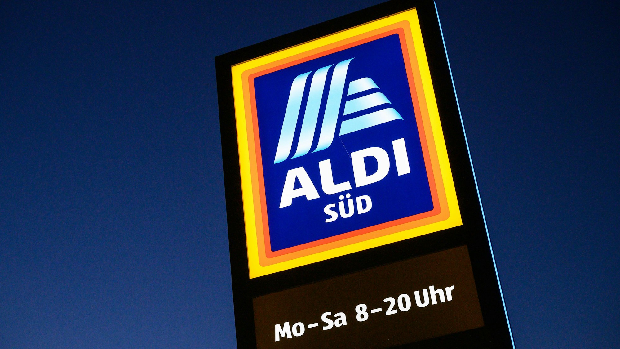 Ein Schild des Discounters Aldi Süd leuchtet in der Dämmerung.