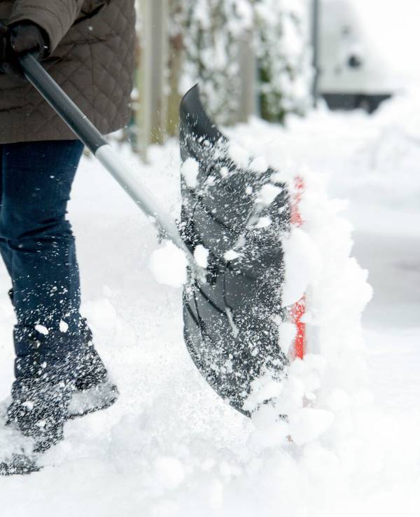 Eine Frau räumt mit einer Schneeschaufel den Schnee beiseite, um ihrer Räumpflicht nachzukommen.