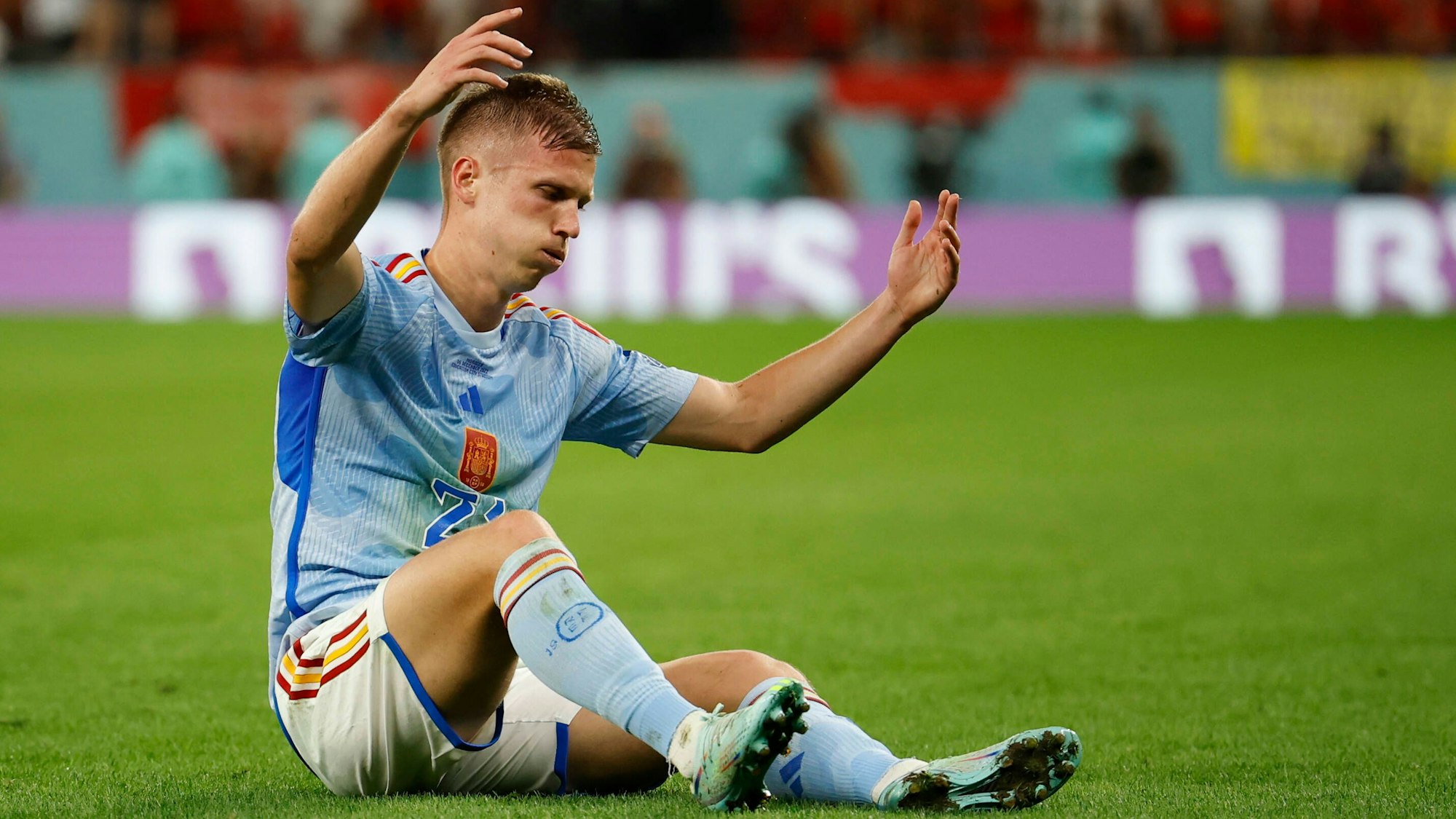 Spaniens Nationalspieler Dani Olmo sitzt enttäuscht auf dem Rasen.