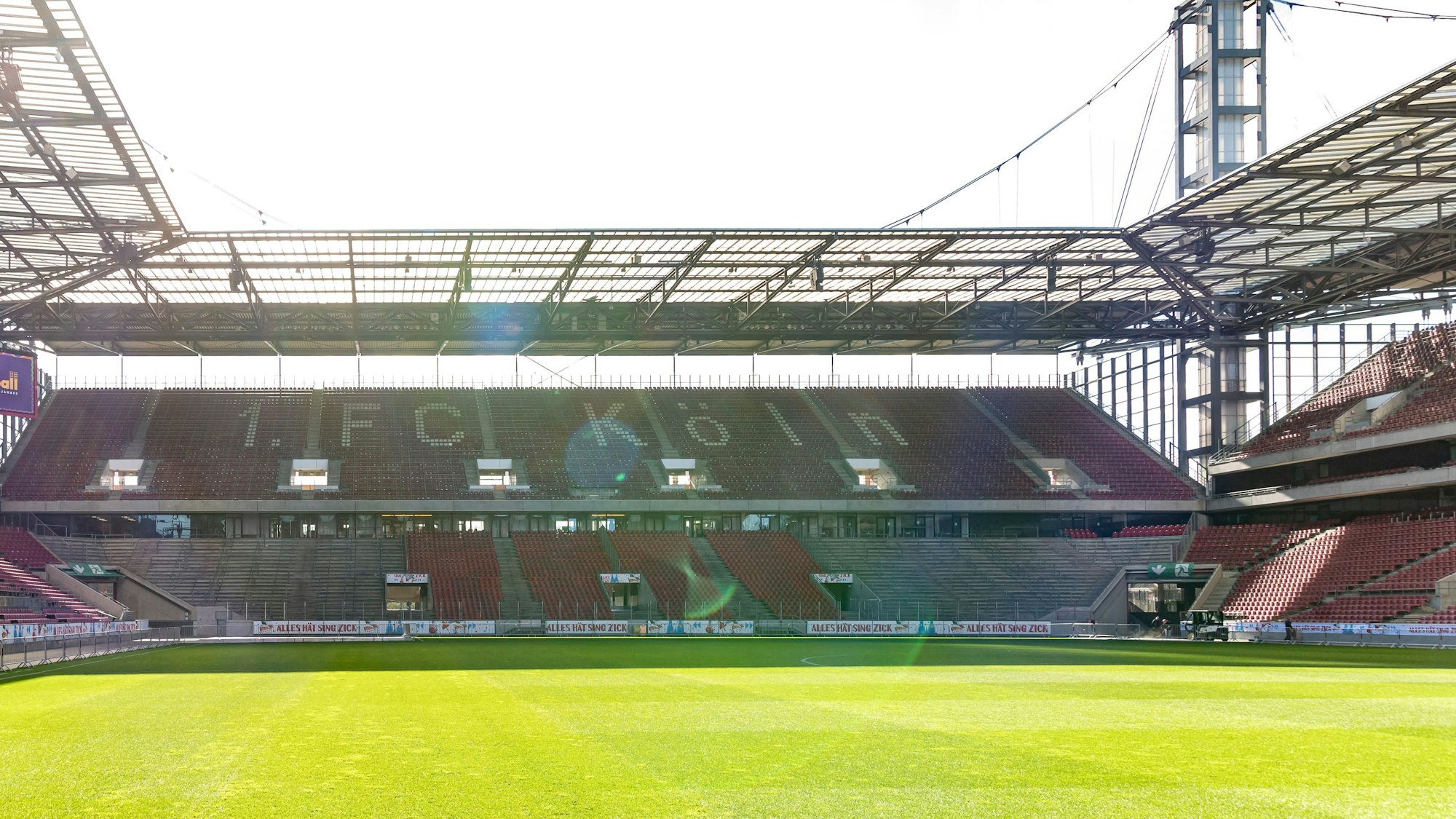 Innenansicht des Rhein-Energie-Stadions in Köln. Die Zuschauerplätze sind leer, die Sonne scheint.