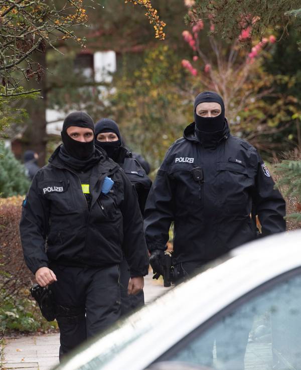 Drei maskierte Polizistinnen und Polizisten laufen in Uniform zu ihrem Auto.