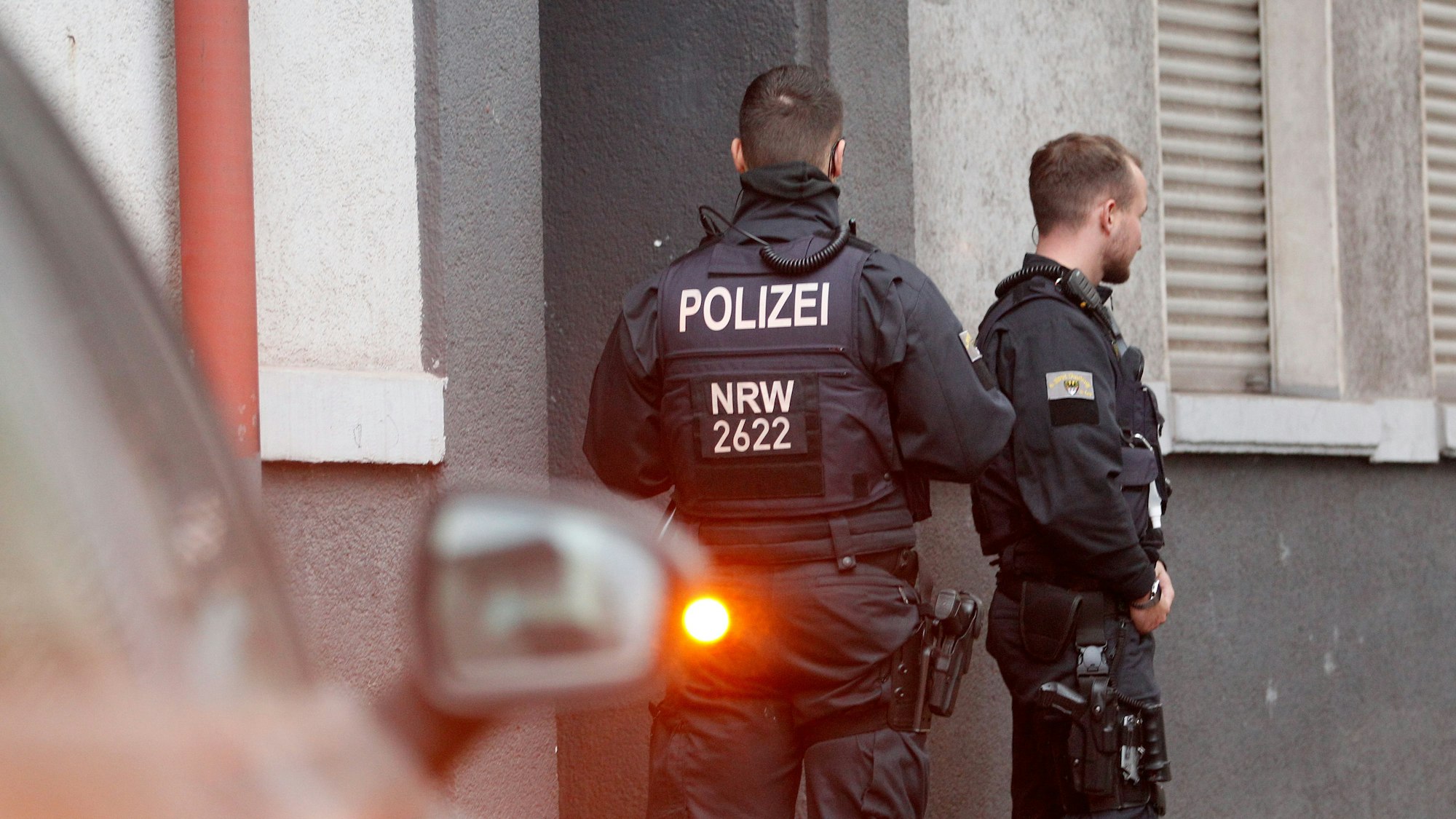 Polizisten stehen vor einem Haus, in dem sie eine Wohnung durchsucht haben.