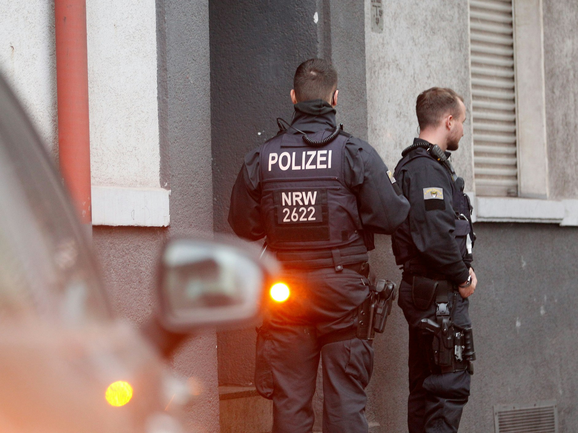 Polizisten stehen vor einem Haus, in dem sie eine Wohnung durchsucht haben.