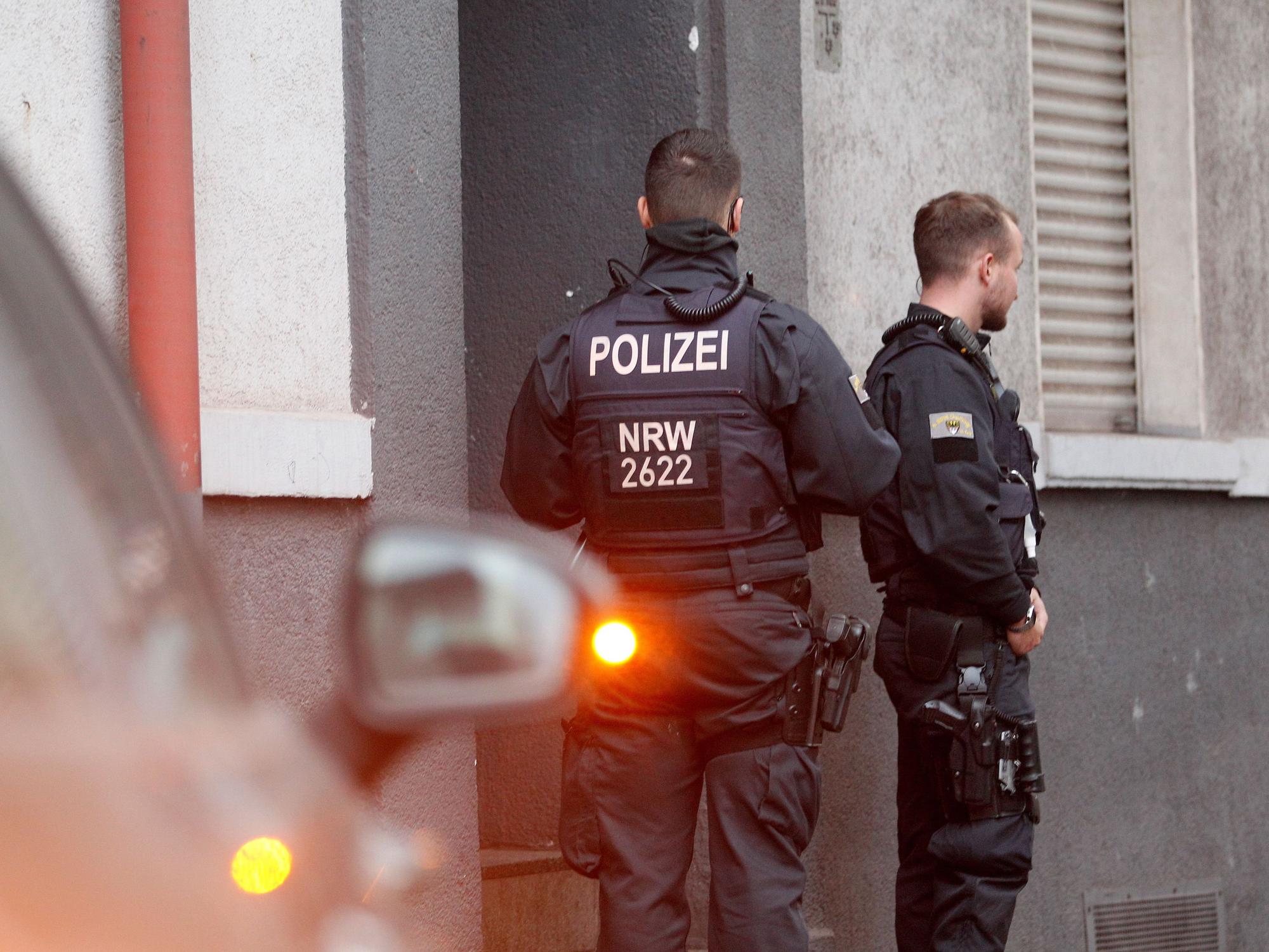 Polizisten stehen vor einem Haus, in dem sie eine Wohnung durchsucht haben.