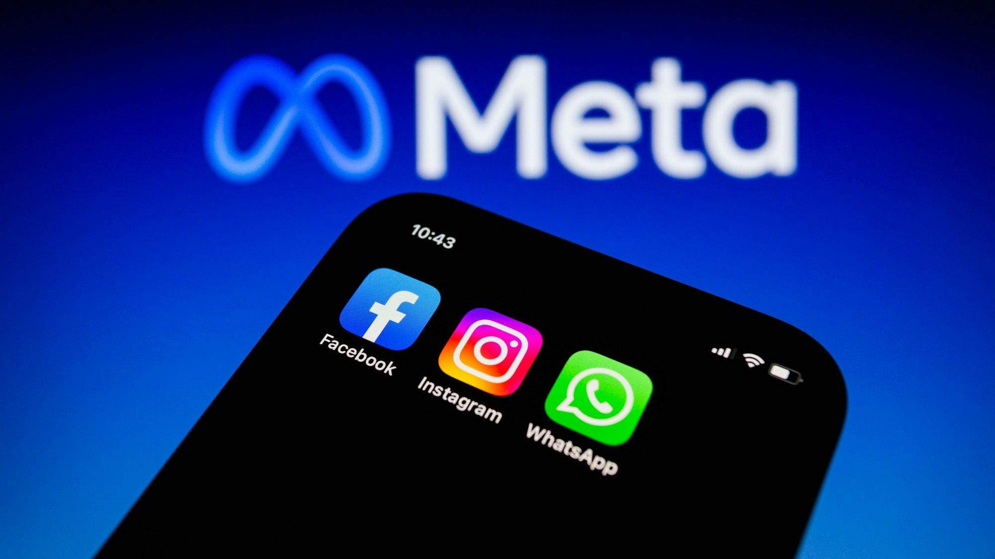 Die Apps von Facebook, Instagram und WhatsApp sind auf einem Smartphone vor dem Logo von Meta Platforms zu sehen.