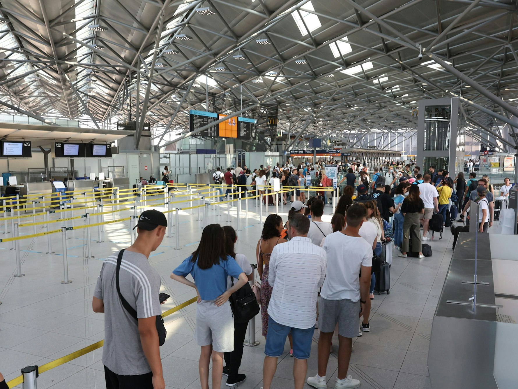 Menschen warten in einer großen Schlange am Flughafen Köln/Bonn an der Sicherheitskontrolle.