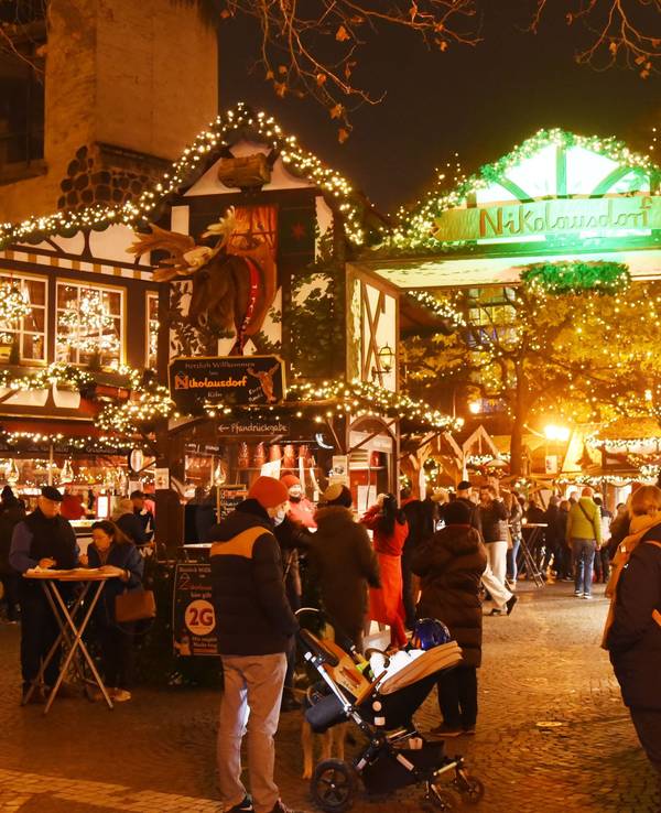 Auf dem Weihnachtsmarkt auf dem Kölner Rudolfplatz stehen viele Menschen und trinken Glühwein oder Punsch. Andere essen oder laufen über den Markt.