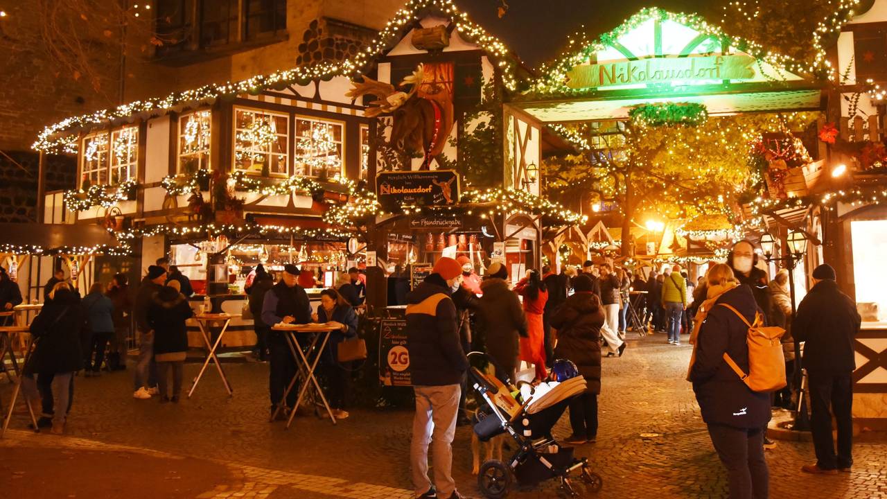Auf dem Weihnachtsmarkt auf dem Kölner Rudolfplatz stehen viele Menschen und trinken Glühwein oder Punsch. Andere essen oder laufen über den Markt.