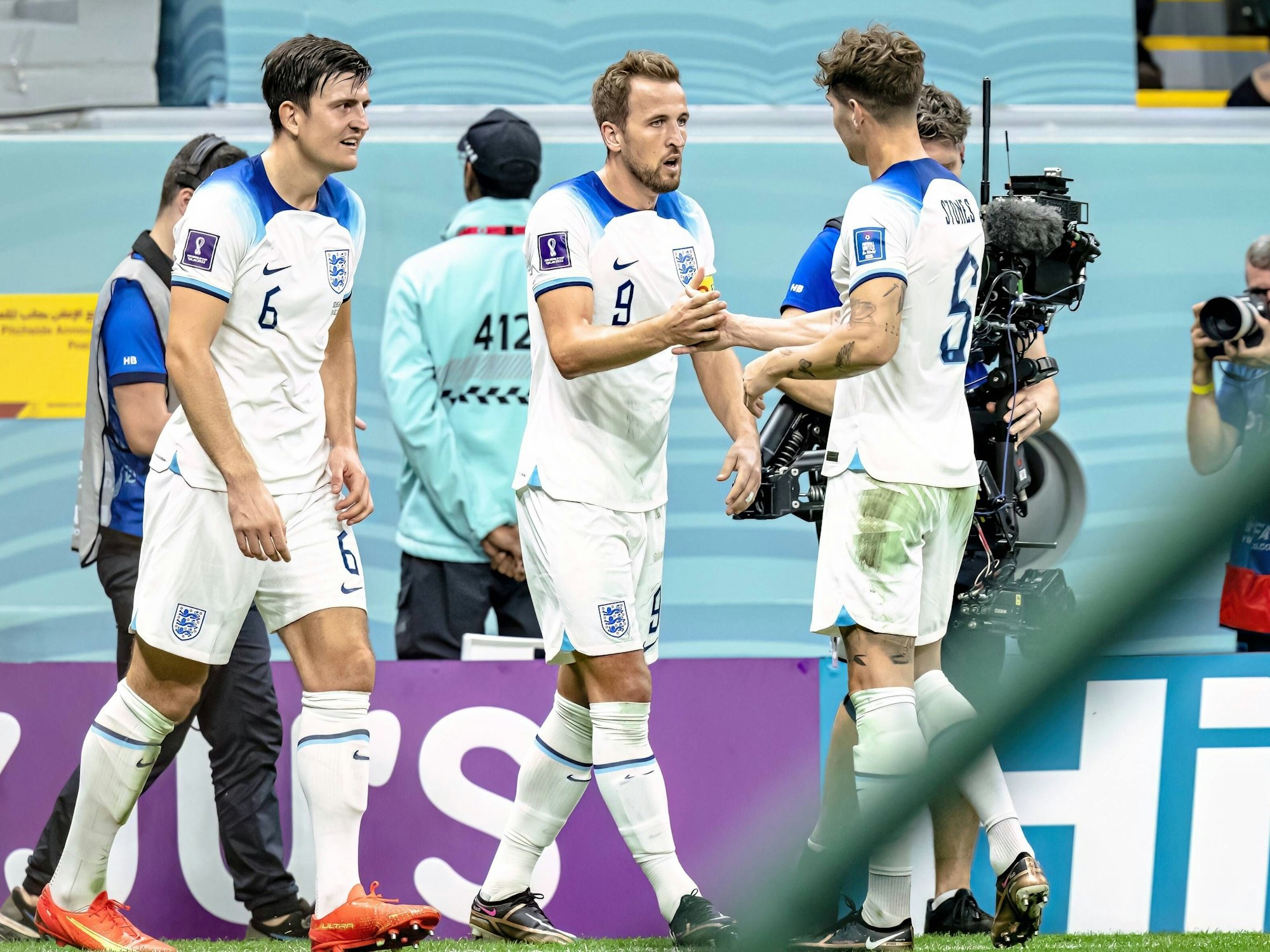Harry Maguire (l.) und John Stones (r.) jubeln mit Englands Torschütze Harry Kane nach dessen 2:0 im WM-Achtelfinale von Katar gegen den Senegal.