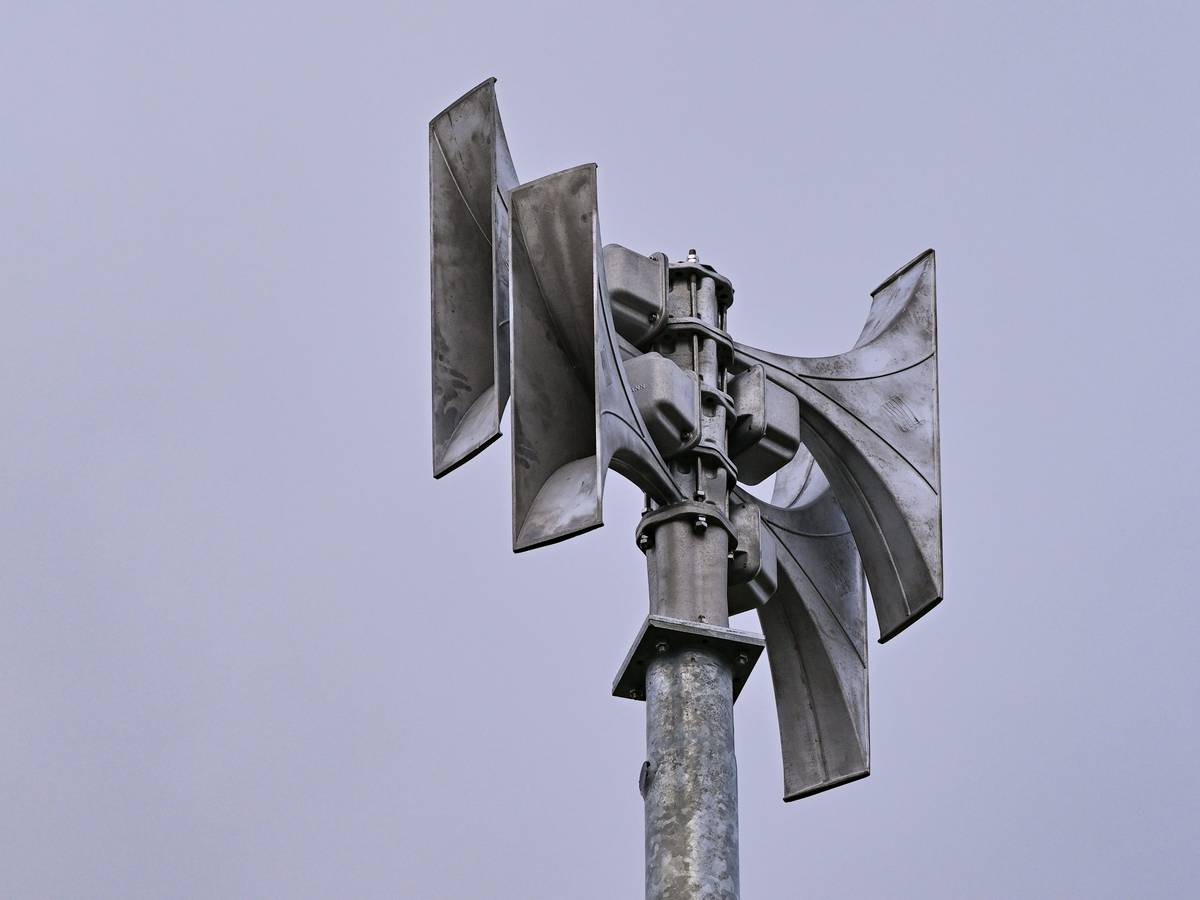 Eine Sirene aus Metall vor blauem Himmel.