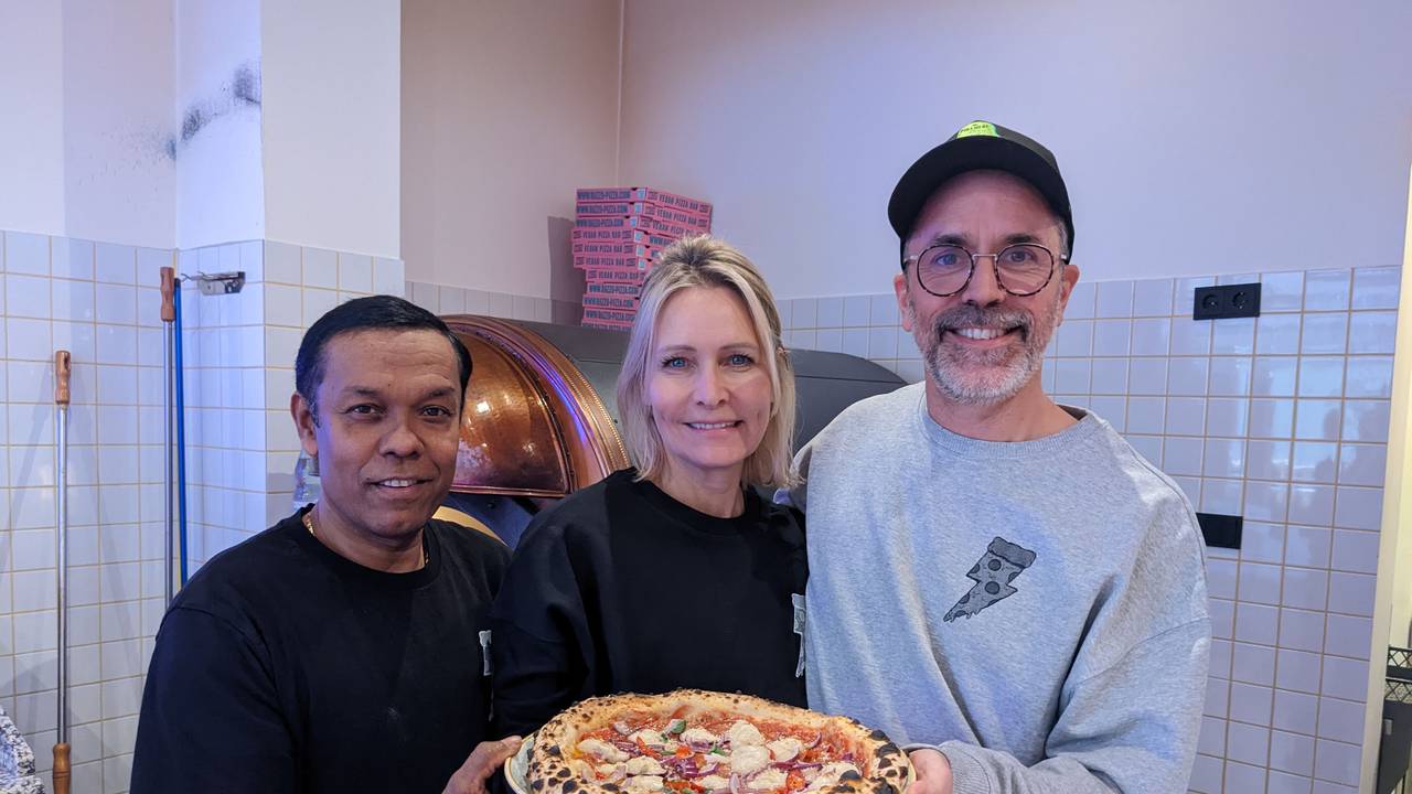Pizzabäcker Monir (l.) posiert am 8. Dezember 2022 mit Chefin Verena Malta und Chef Ingo Noack. Sie halten einen Teller, auf dem sich eine vegane Pizza befindet.