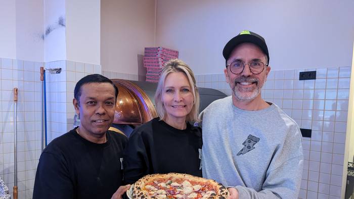 Pizzabäcker Monir (l.) posiert am 8. Dezember 2022 mit Chefin Verena Malta und Chef Ingo Noack. Sie halten einen Teller, auf dem sich eine vegane Pizza befindet.