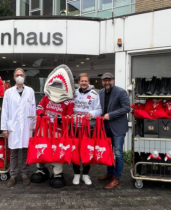 Professor Michael Weiß, Sharky, KEC-Kapitän Moritz Müller sowie Haie-Geschäftsführer Philipp Walter mit den Geschenken vor der Kinderklinik.