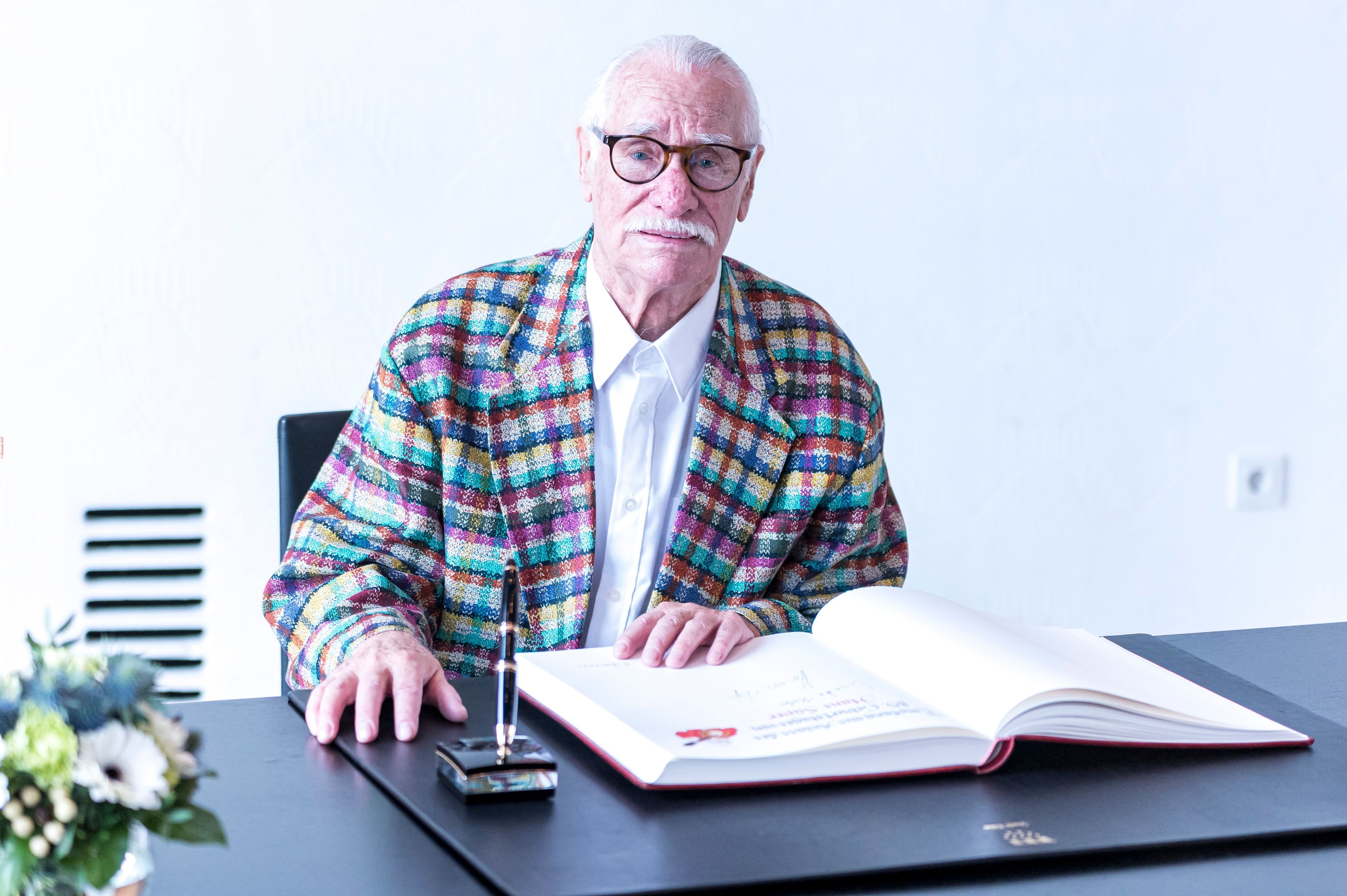 Hans Süper trägt sich ins Gästebuch der Stadt Köln ein und schaut in die Kamera.