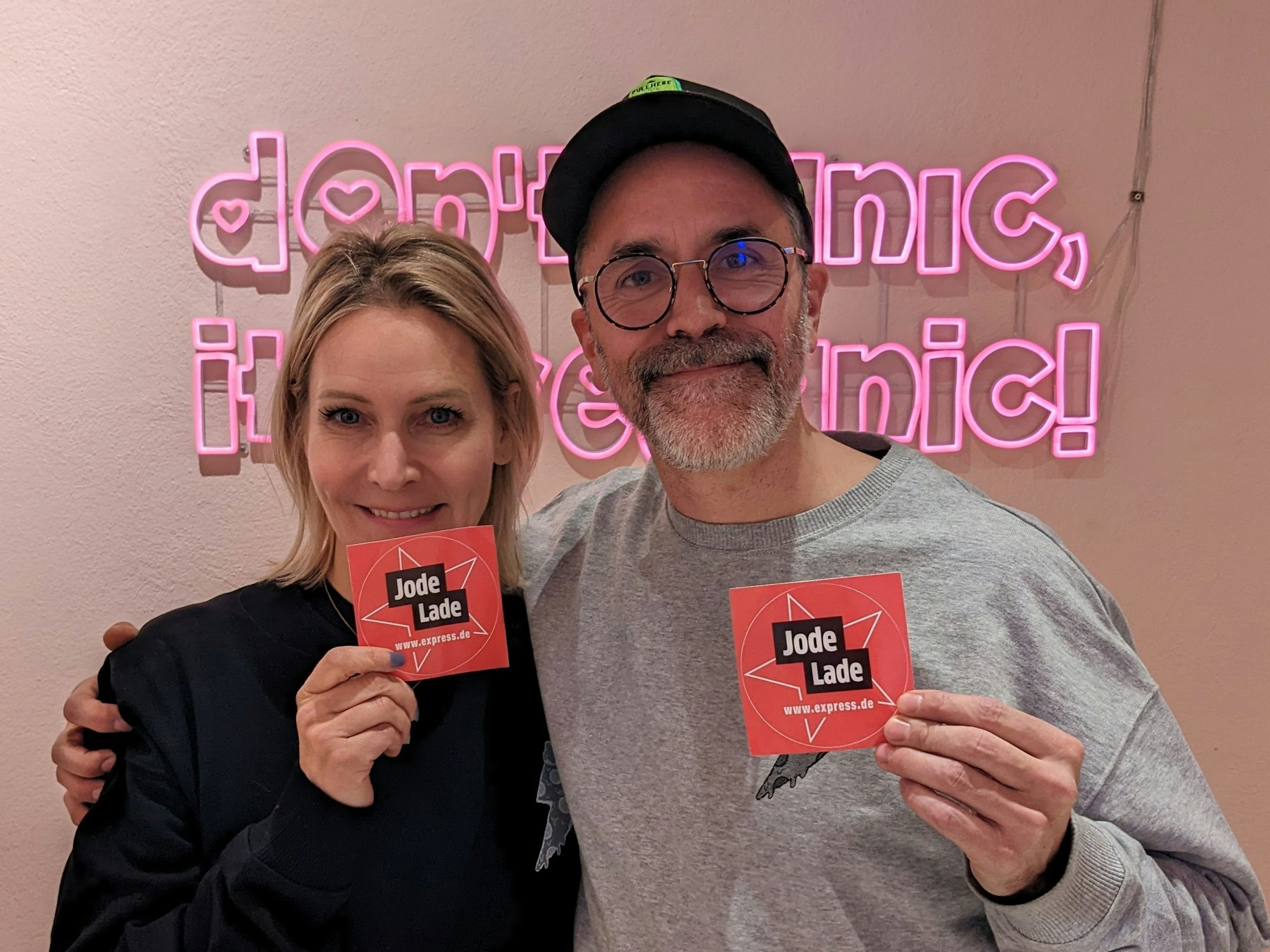 Verena Malta und Ingo Noack vom Razzo halten „Jode Lade“-Sticker hoch. Diese Auszeichnung haben sie von EXPRESS.de von erhalten. Im Hintergrund ist der Slogan „Don't panic, it's veganic“ zu lesen.