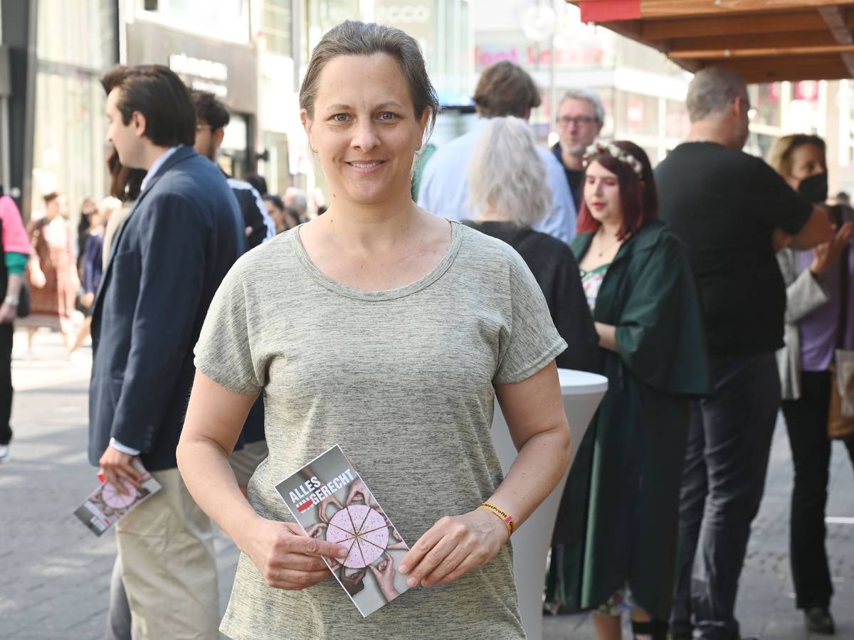 Nicolin Gabrysch steht mit einem Wahlzettel in der Hand in Köln auf der Straße und lächelt in die Kamera.