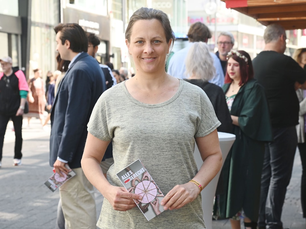 Nicolin Gabrysch steht mit einem Wahlzettel in der Hand in Köln auf der Straße und lächelt in die Kamera.