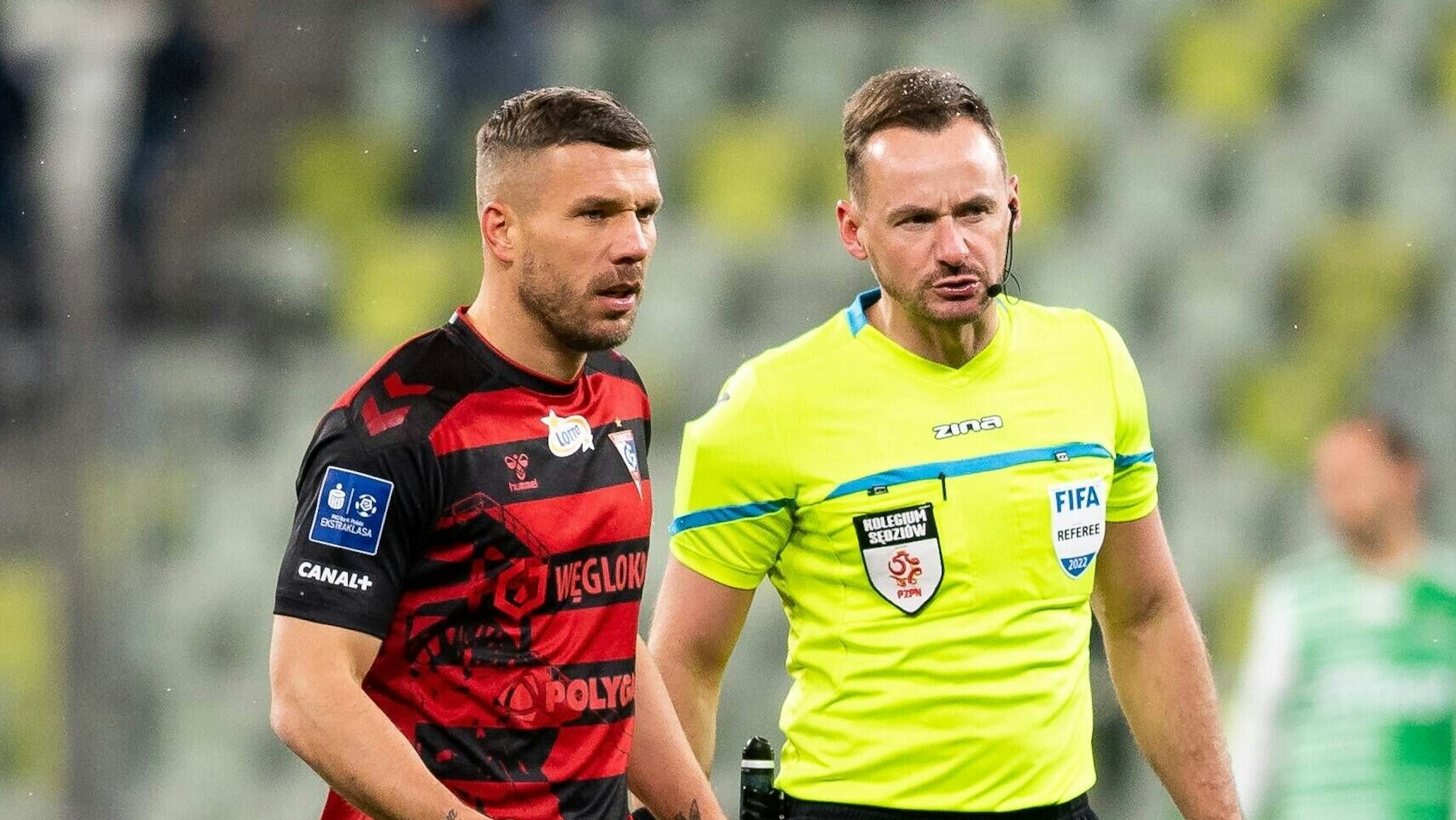 Lukas Podolski im Auswärtstrikot von Gornik Zabrze neben Schiedsrichter Pawel Raczkowski.