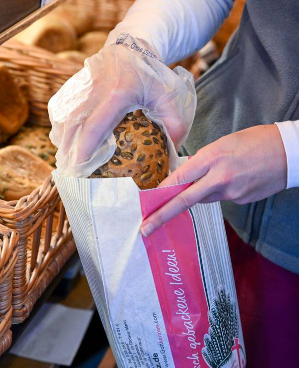 Eine Person packt ein Körnerbrötchen in eine Papiertüte in einer Bäckerei.